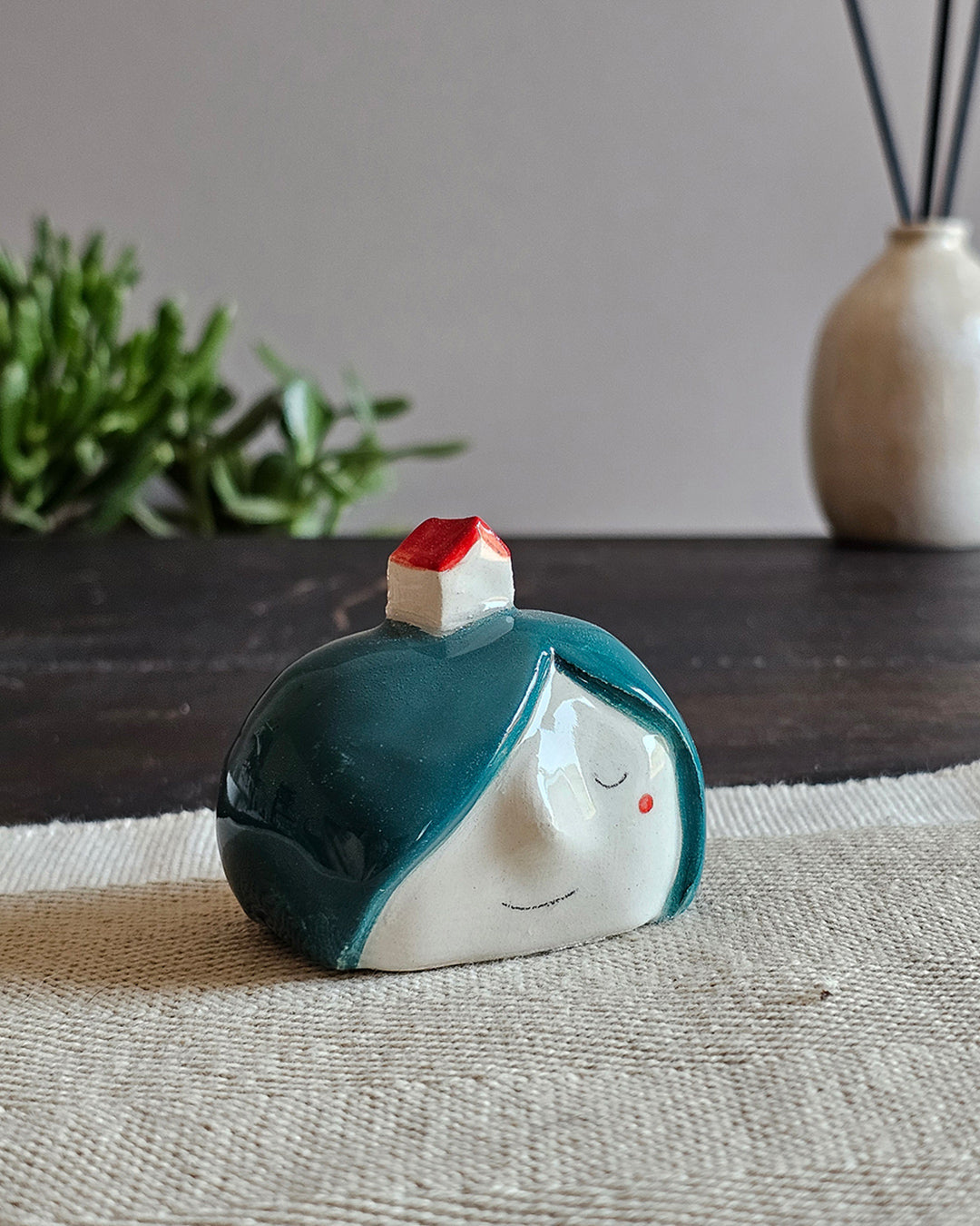 Testina in ceramica bianca con una casetta dal tetto storto appoggiata in testa