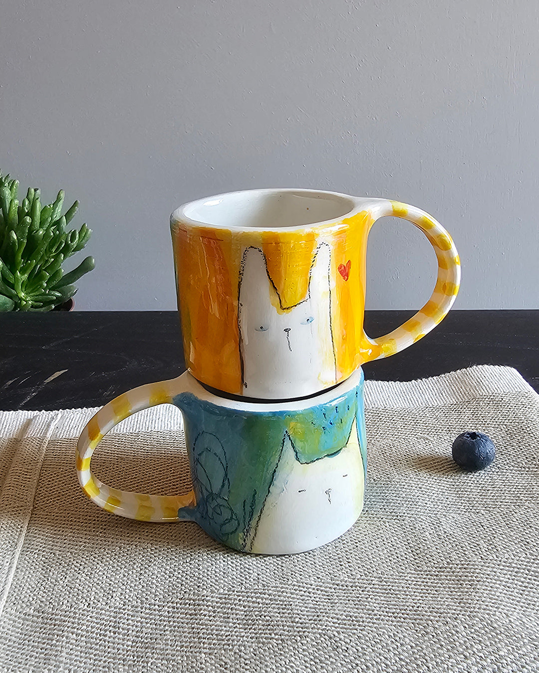Due tazzine in ceramica, una blu e una gialla, con animali innamorati modellati a mano