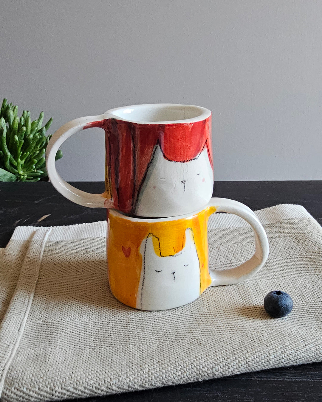 Due tazzine in ceramica, una rossa e una gialla, con animali innamorati modellati a mano