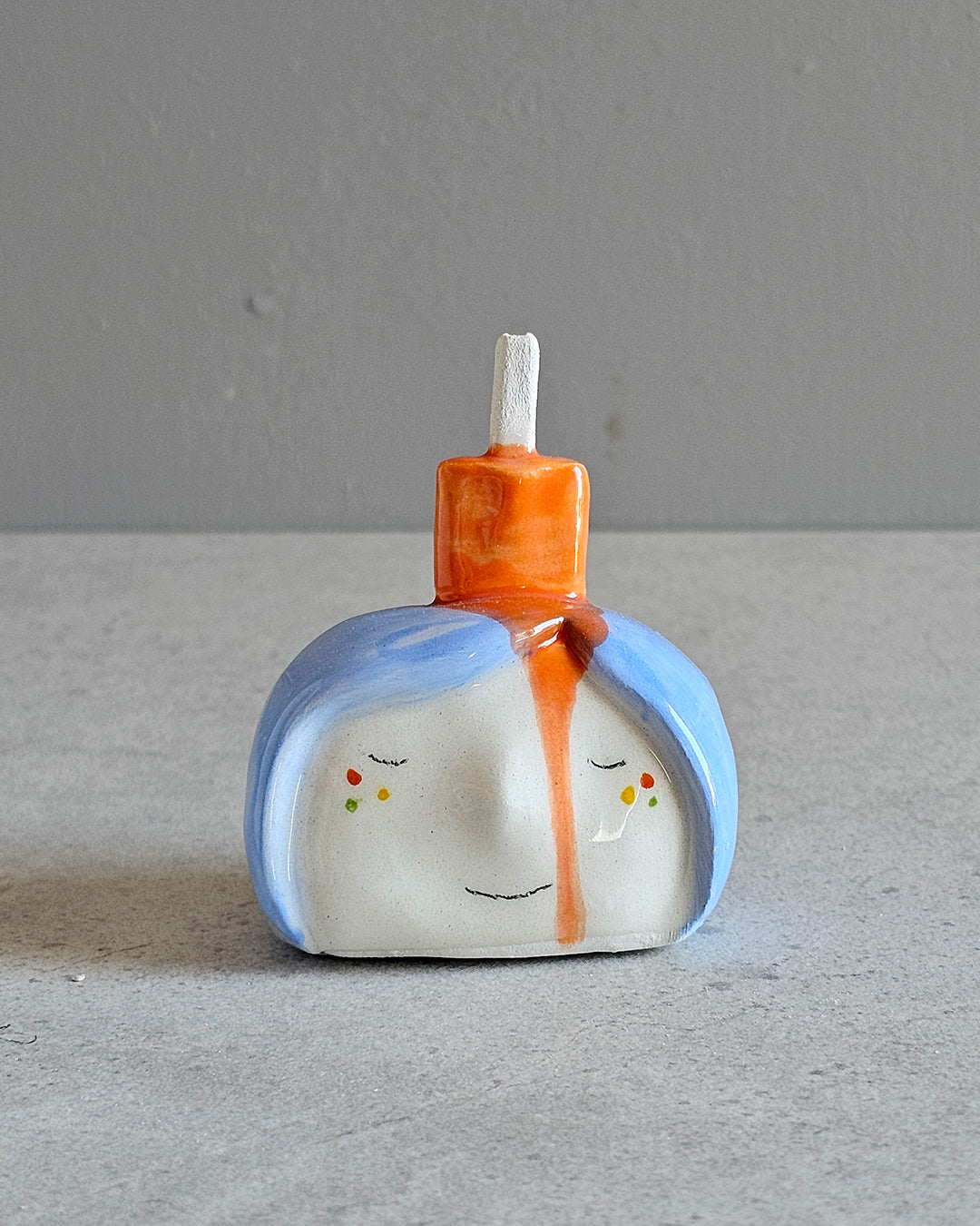 Testina in ceramica bianca con un ghiacciolo arancione che cola sui capelli