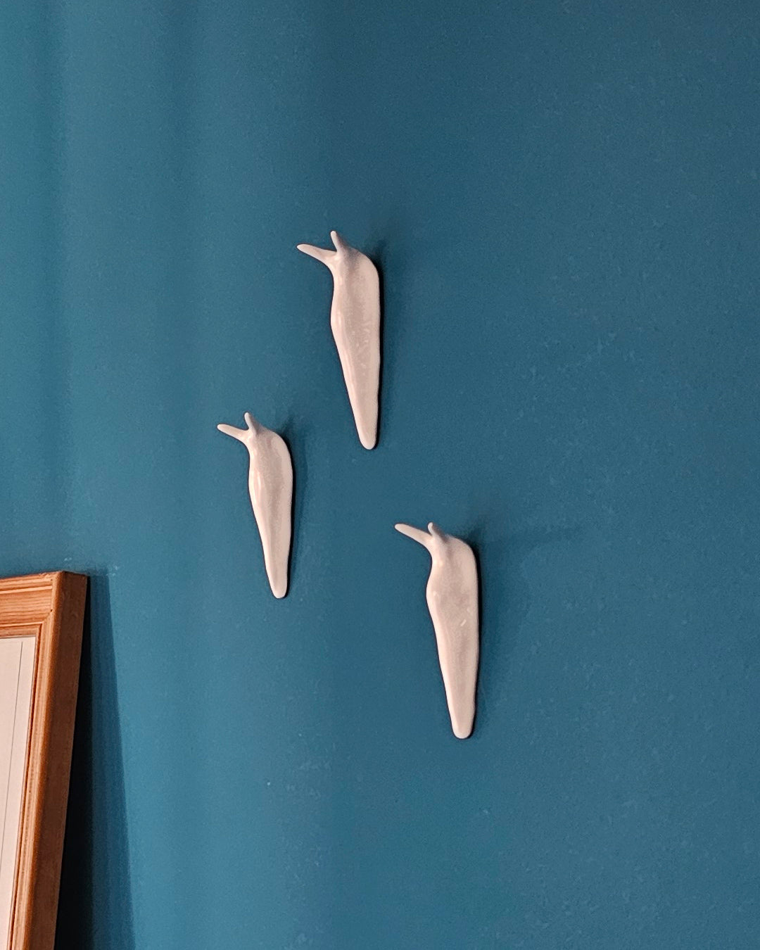 Tre lumache in ceramica bianca appese al muro, modellate a mano