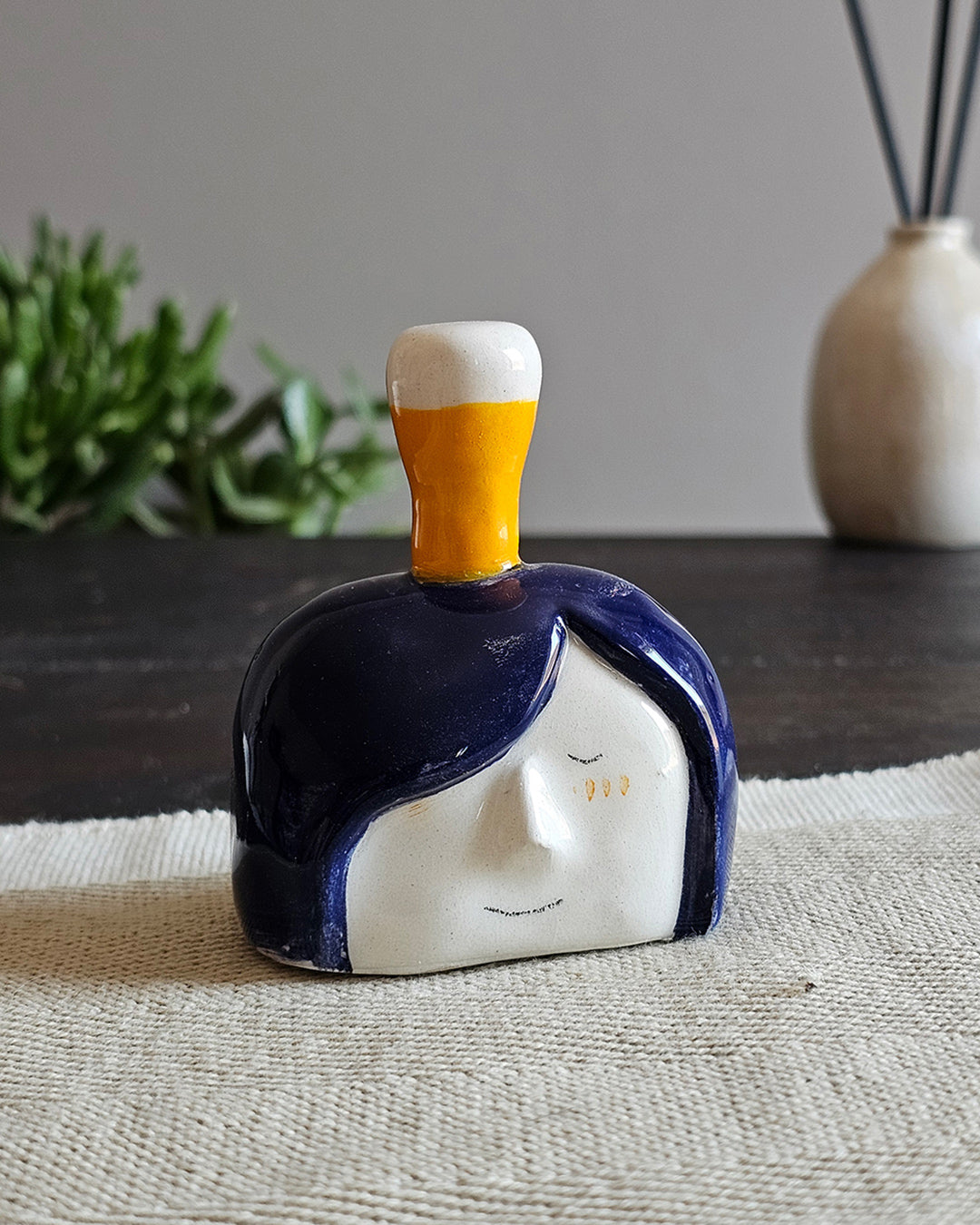 Testina in ceramica bianca con una birra alta appoggiata in testa, fatta a mano