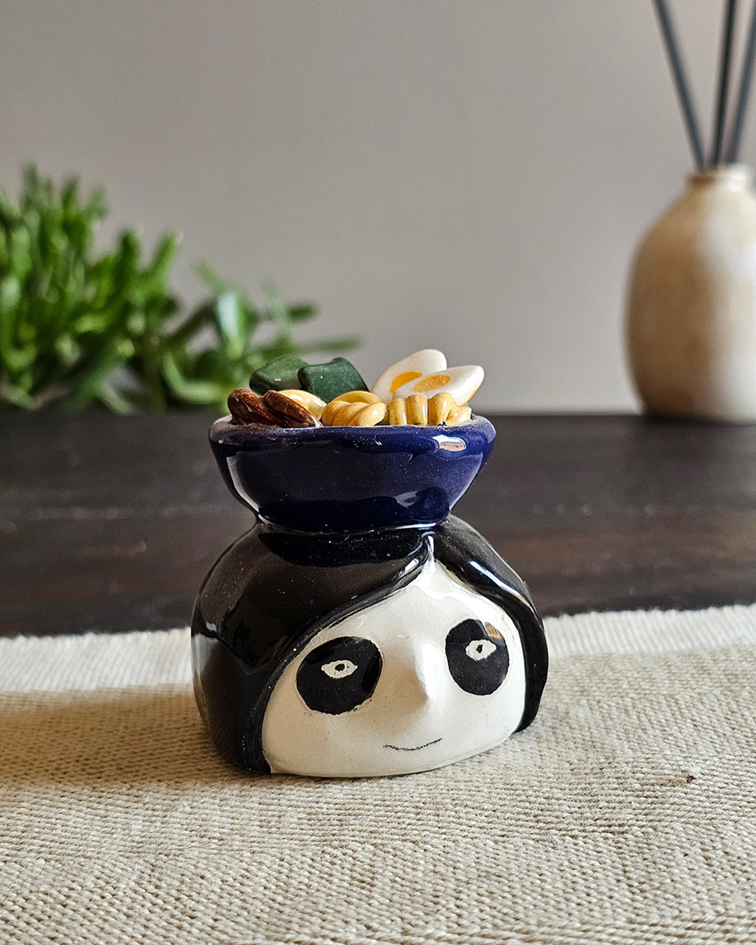 Testina in ceramica bianca con una ciotola di ramen appoggiata in testa
