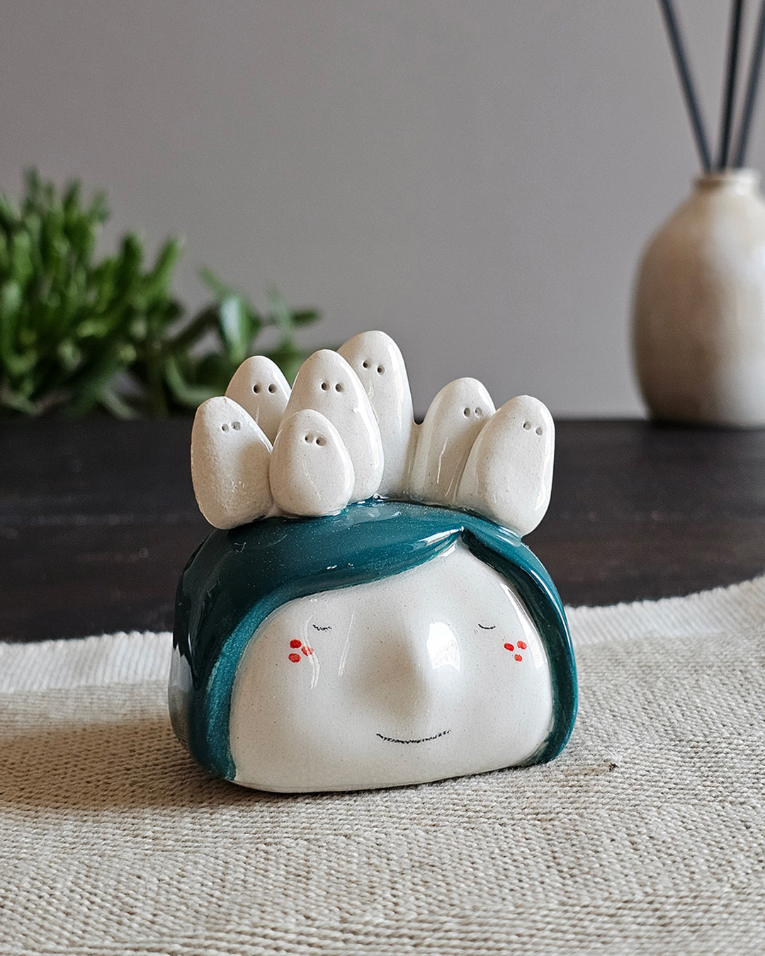 Testina in ceramica bianca con sette fantasmini seduti in fila sui capelli