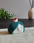 Testina in ceramica bianca con una casetta dal tetto storto appoggiata in testa