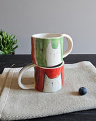 Due tazzine in ceramica, una rossa e una verde, con animali innamorati modellati a mano