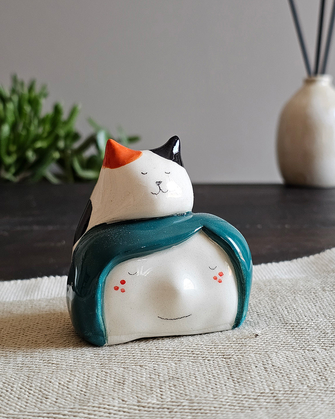 Testina in ceramica bianca con un gatto tricolore seduto in testa, fatta a mano