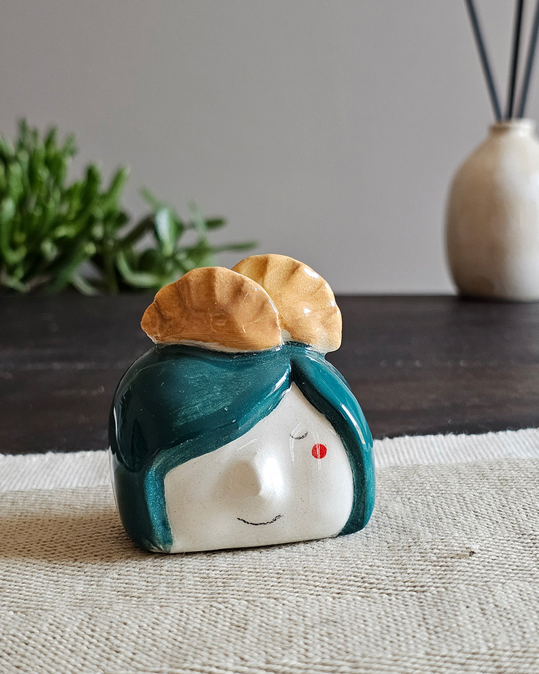 Testina in ceramica bianca con due gyoza dorati appoggiati in testa, fatta a mano