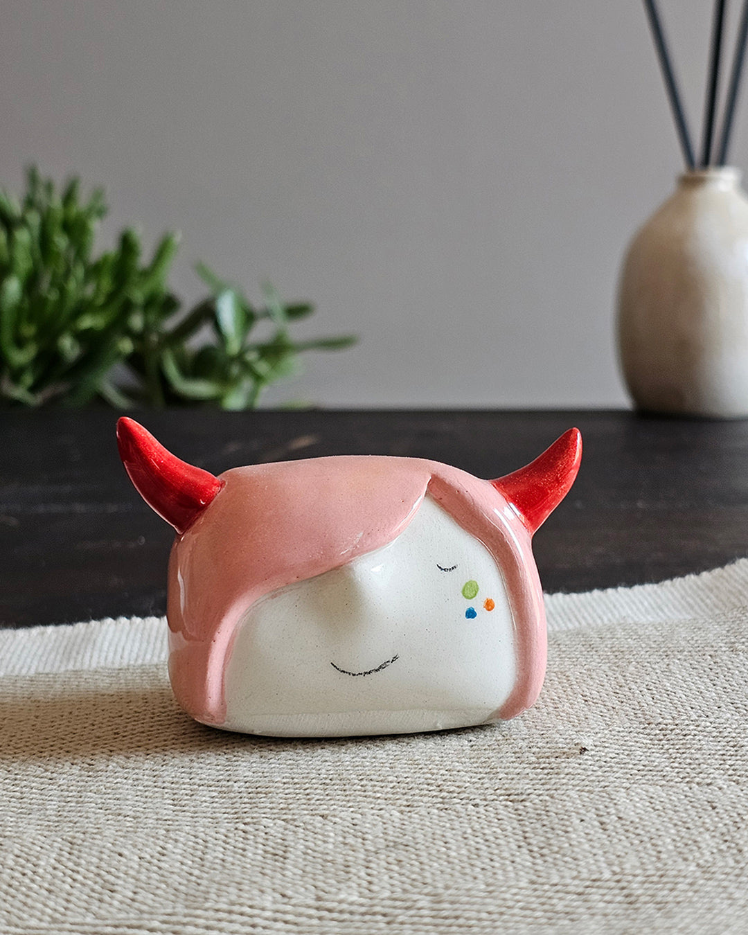 Testina in ceramica bianca con due corna rosse su capelli rosa, fatta a mano