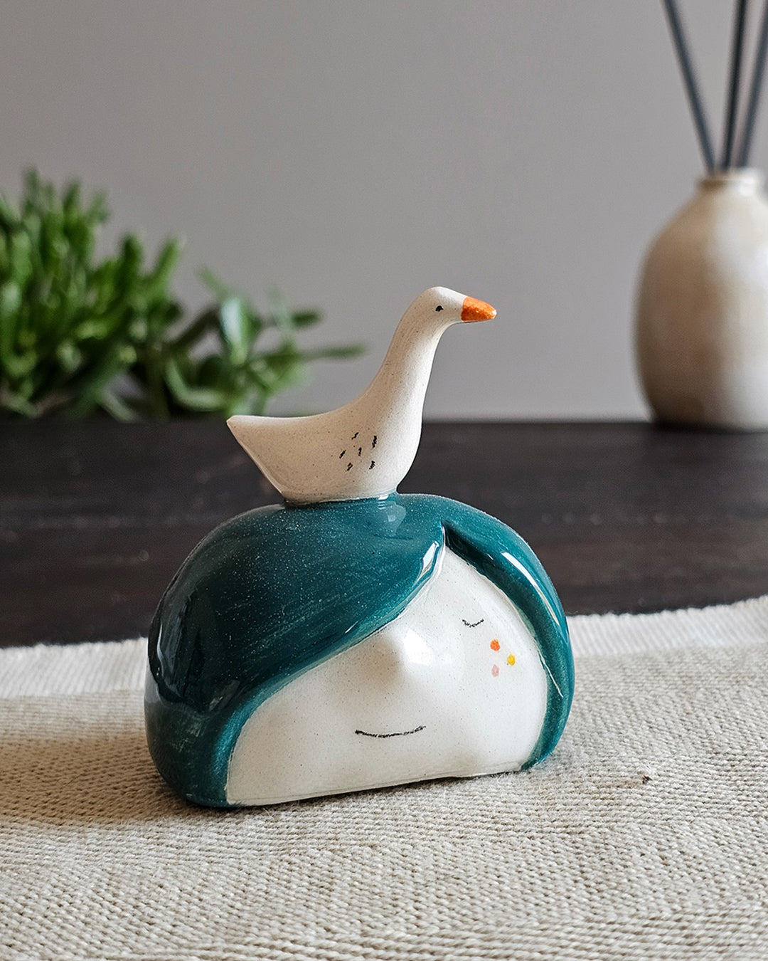 Testina in ceramica bianca con un'oca dal collo teso appoggiata in testa
