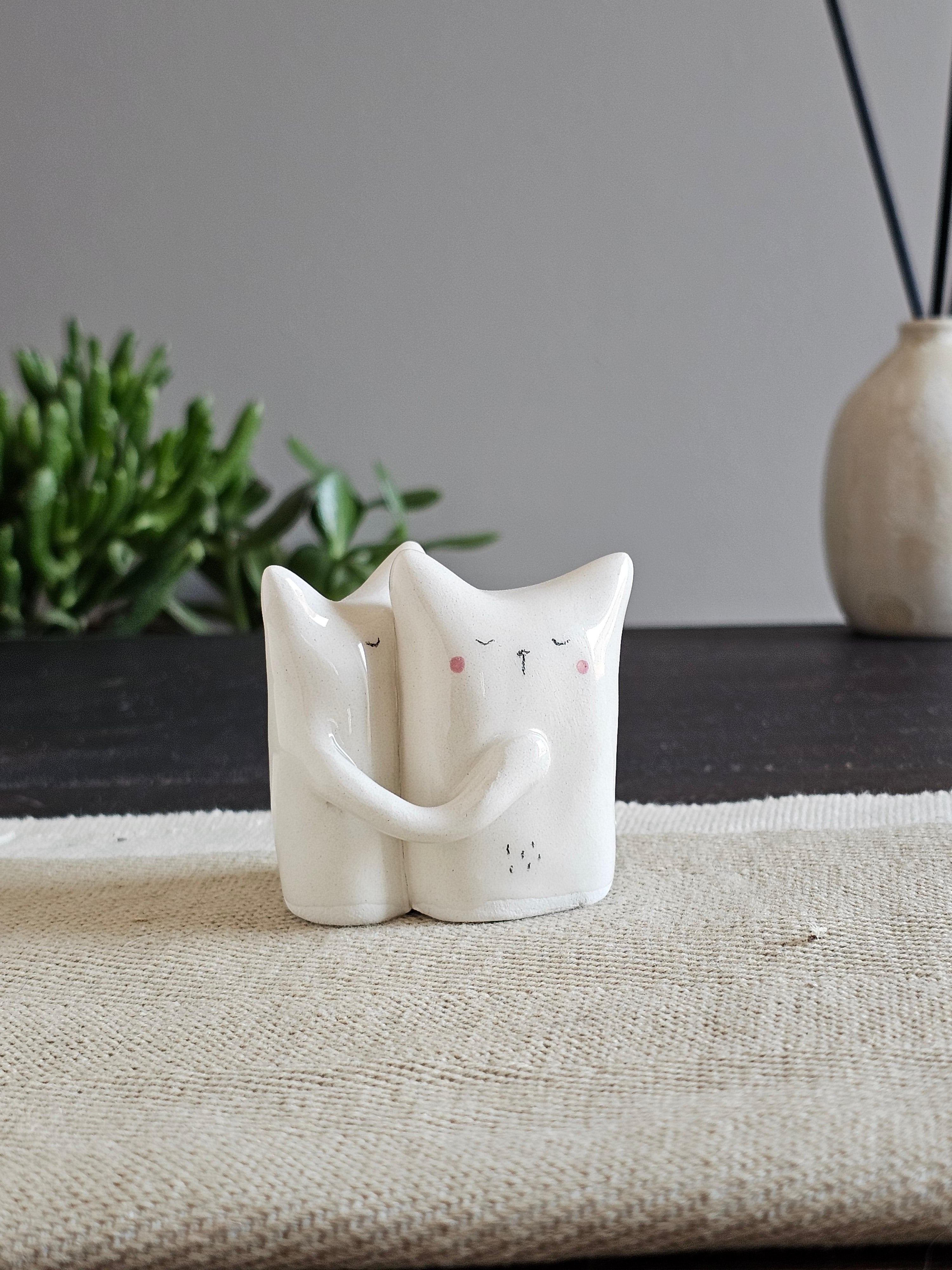 Due animali in ceramica bianca abbracciati, una testa appoggiata sulla spalla dell'altro