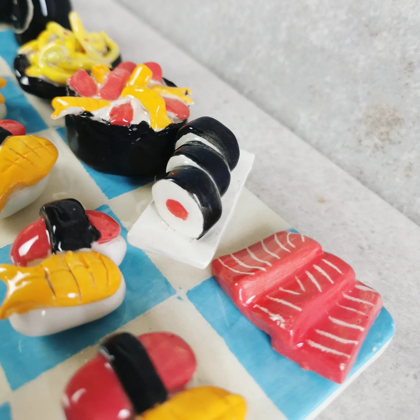 Scacchiera in ceramica con pezzi a forma di sushi e maki, una squadra bianca e una blu